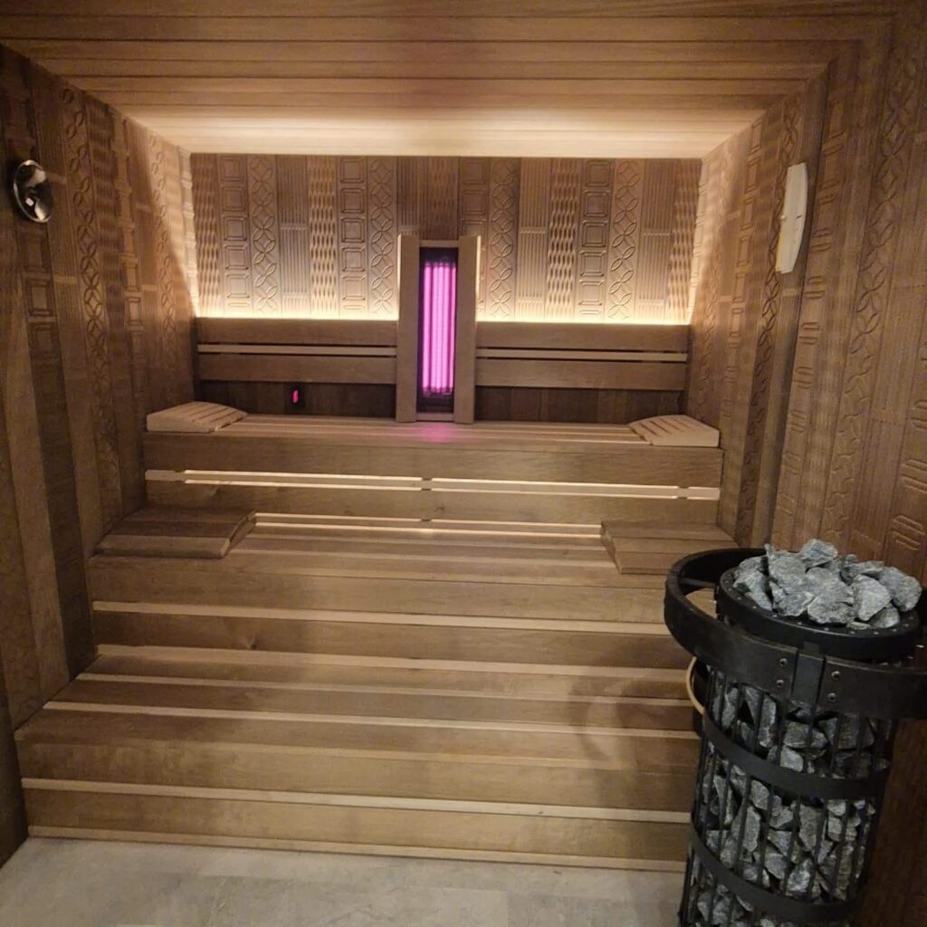 Custom-made indoor sauna with tiered benches and a backlit panel by Nordik Wellness