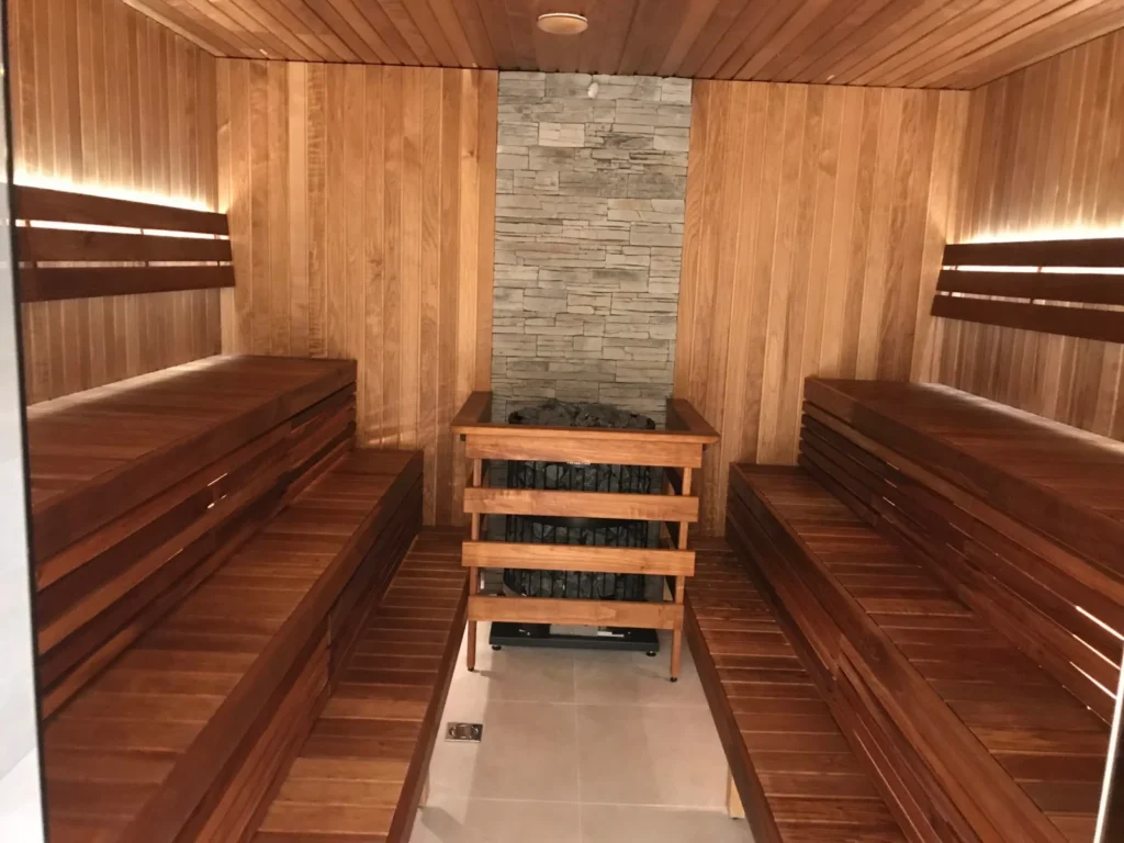 Custom-made indoor sauna with facing bench rows and a stone feature wall by Nordik Wellness