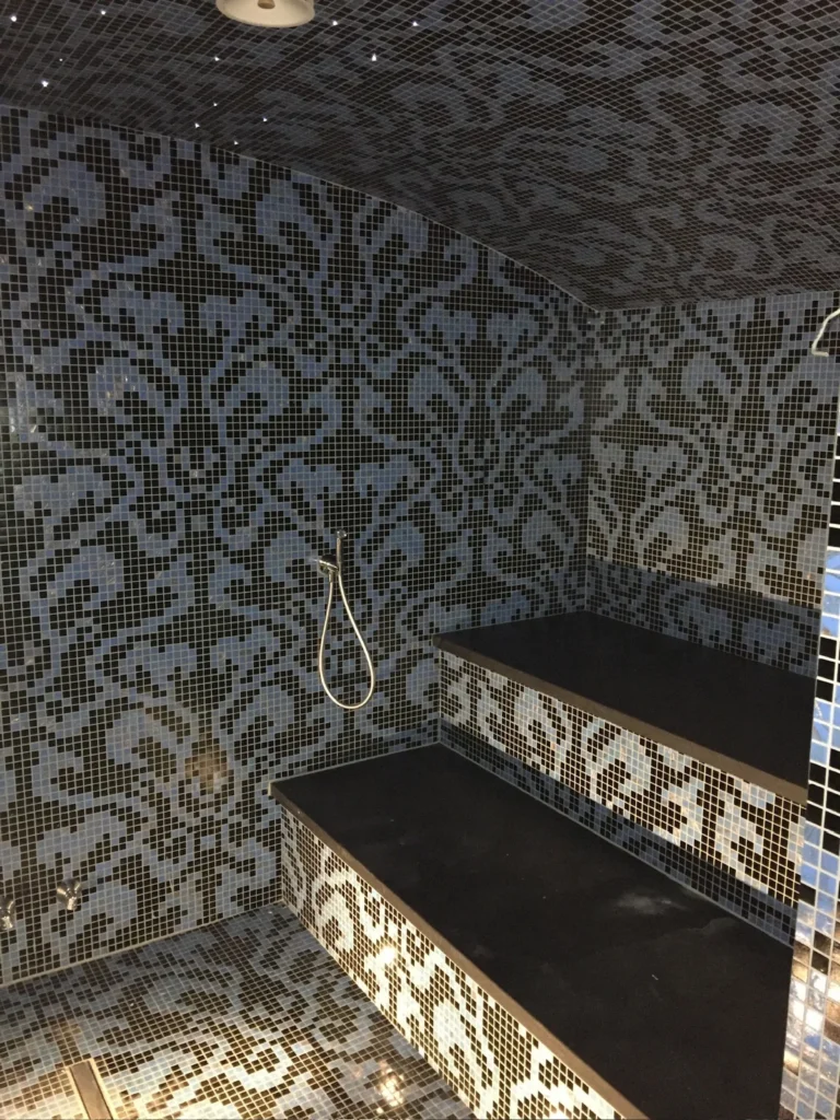 Custom-made indoor steam room with patterned tiling and a black bench by Nordik Wellness