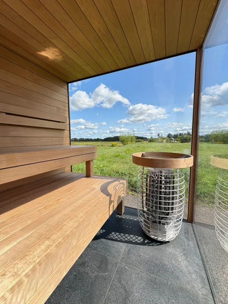 Interior of a new Nordik Wellness outdoor sauna — timber benches, cylindrical heater and a view over open fields