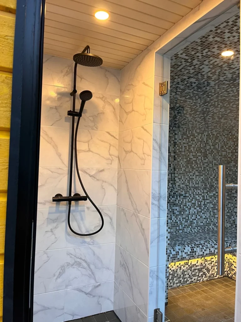 Shower area with a black rain shower and marble-effect tiling beside the glazed steam room