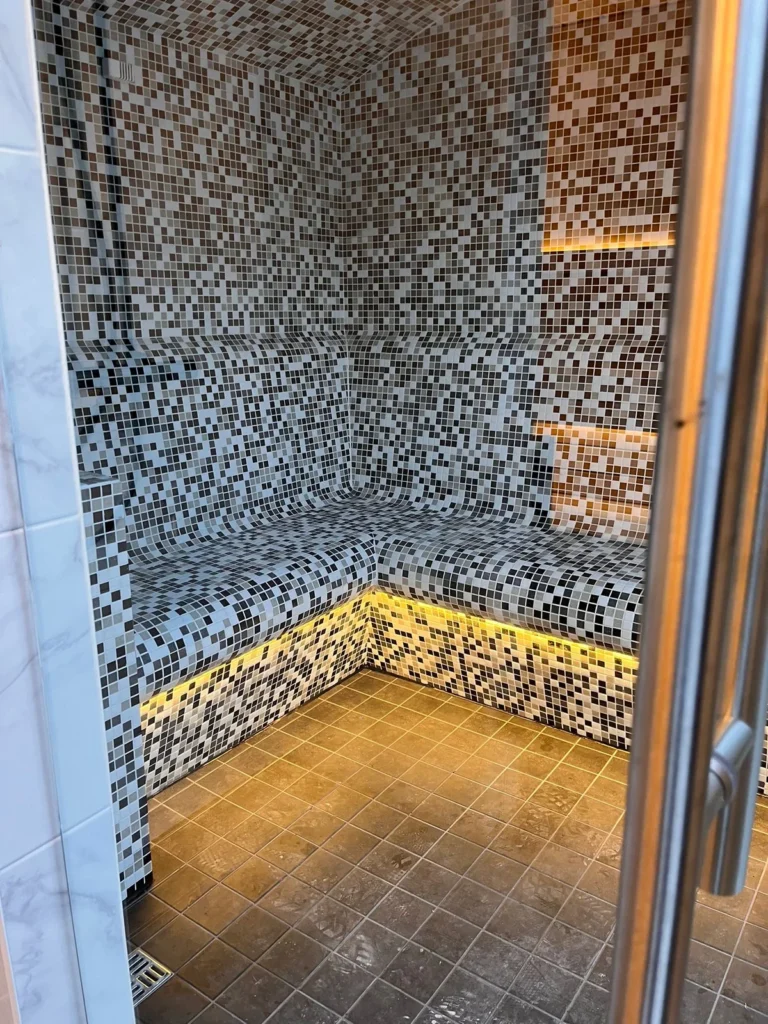 Mosaic-tiled steam room with a contoured seating bench and lit skirting