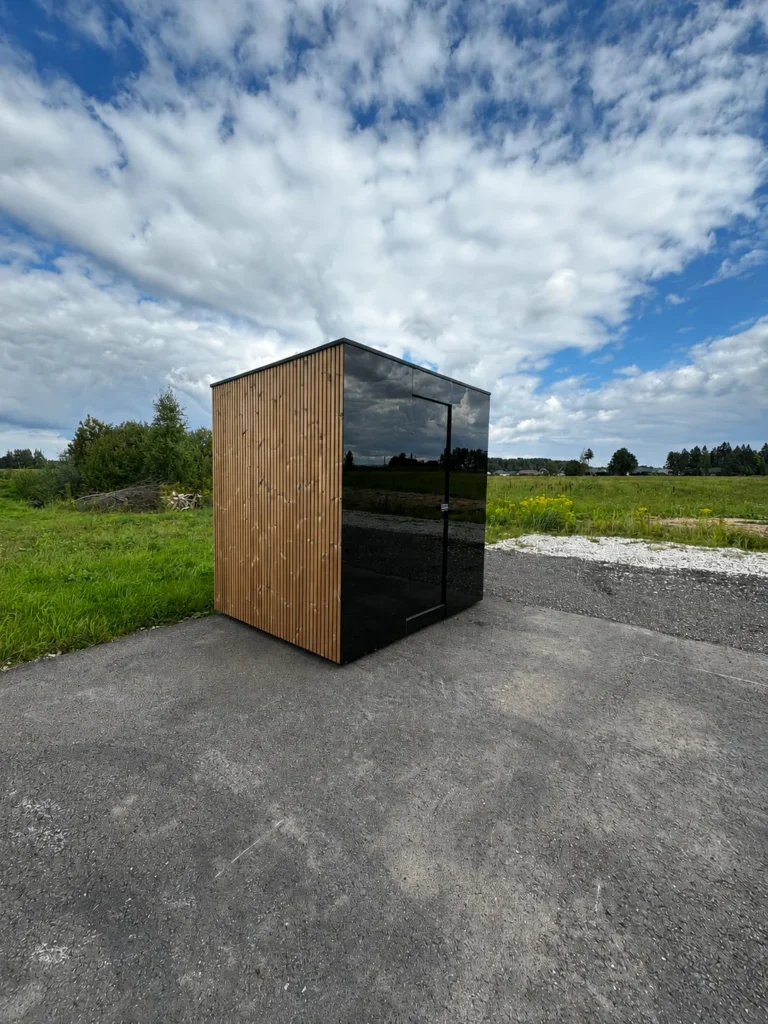 Signature M outdoor sauna, its dark glazed facade reflecting the sky